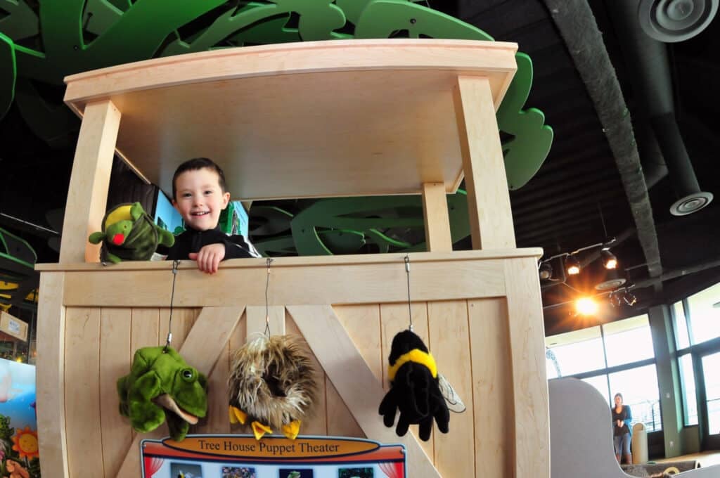 A boy is playing with a puppet in a play set at Betty Brinn Children's Museum.