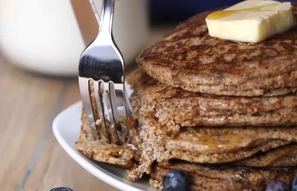 Stack of whole-grain pancakes with butter and syrup and a fork cutting in.