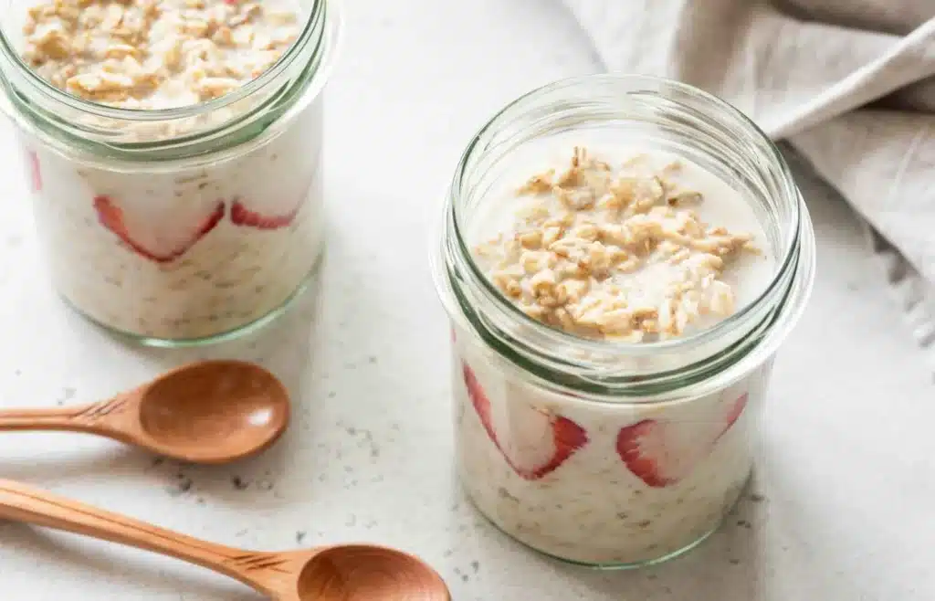 Low-sugar overnight oats in jars with strawberries and creamy milk mixture.