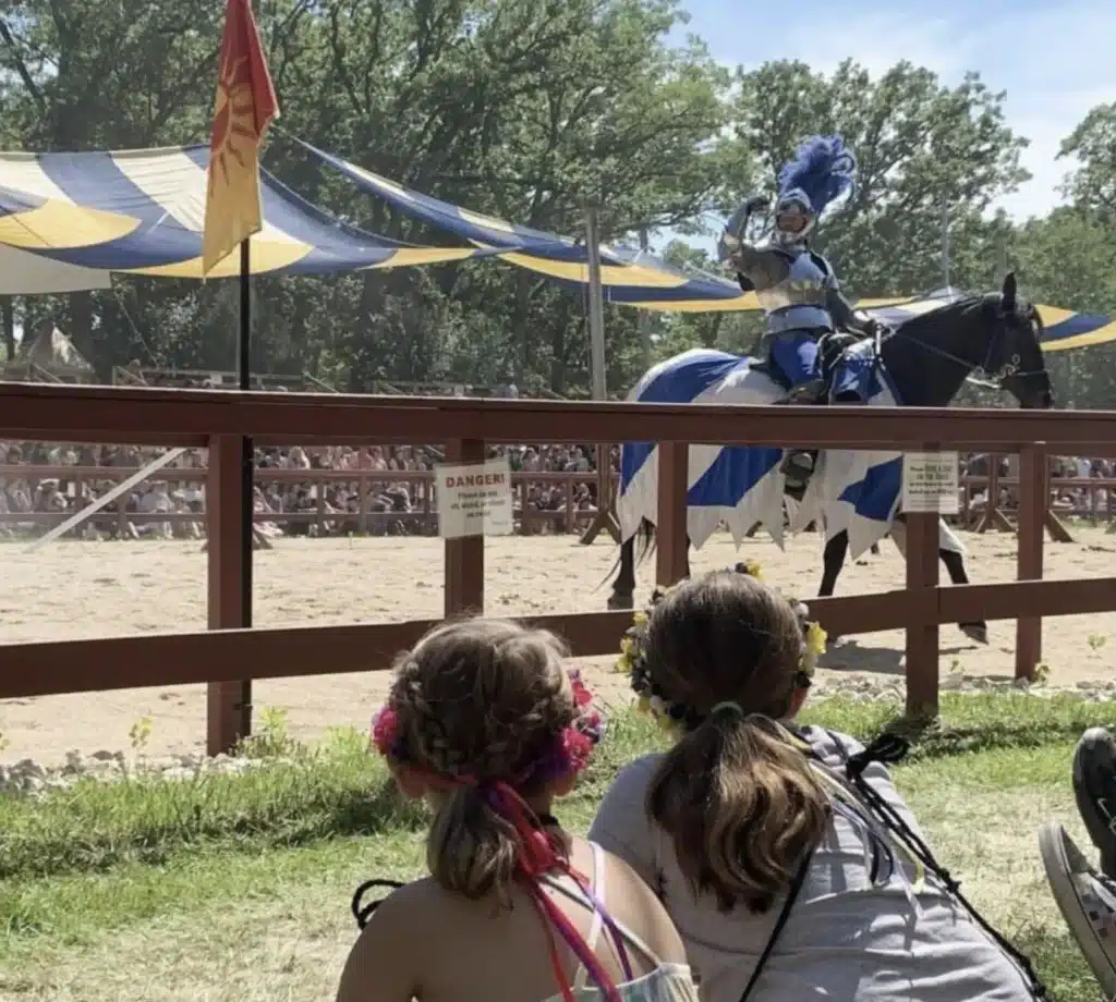 Children wearing flower crowns watching a costumed knight on horseback during a joust at the Bristol Renaissance Faire.