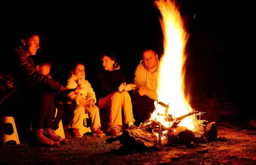 Family sitting around a bright campfire together at night while camping.