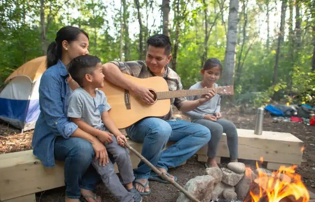 Family sitting by a campfire while a parent plays guitar at the campsite.