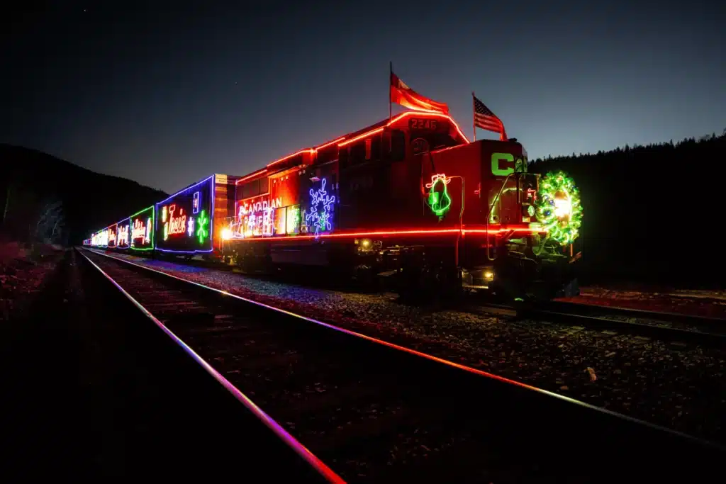 Holiday train is decorated with thousands of Christmas lights while rolling on tracks at dusk