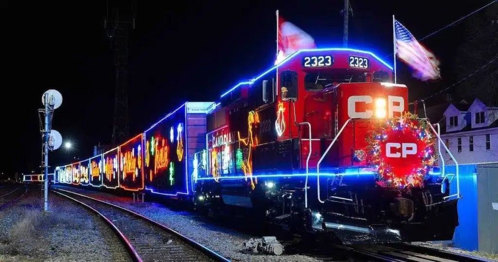 Fully decked-out Canadian Pacific Holiday Train with lights and Canadian and American flags passing a suburban area 