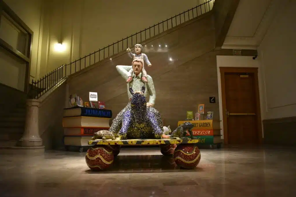 A statue of a father holding his child while riding a giant tortoise with a staircase in the background