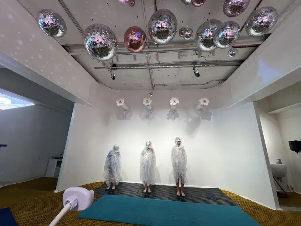 Kids with ponchos stand in the Sloomoo “Get Slimed” zone, surrounded by slime nozzles.