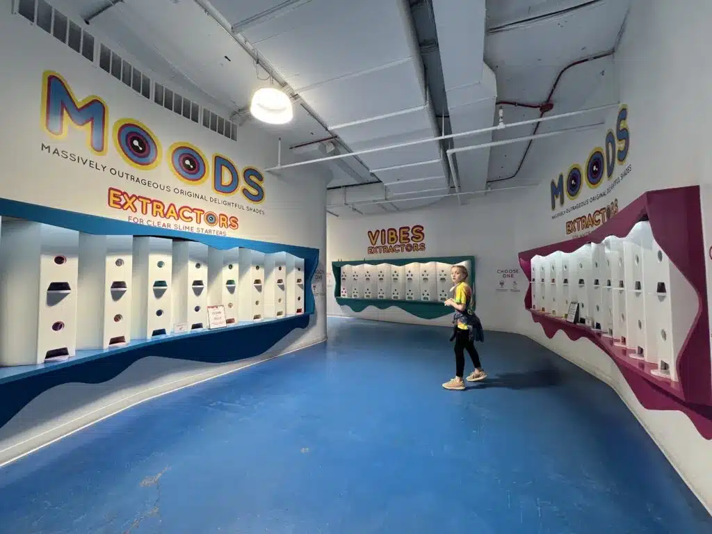 A child stands in front of the Moods and Vibes Extractors wall at Sloomoo Institute Chicago, choosing custom slime.