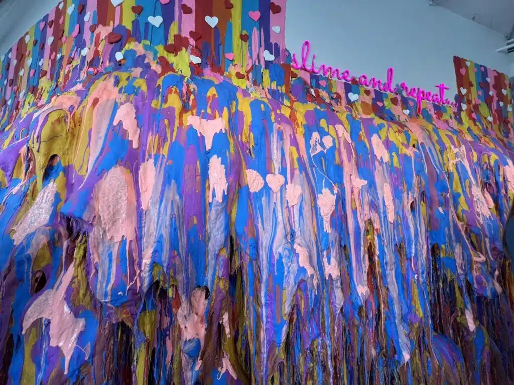 A multicolored slime wall installation at Sloomoo Institute Chicago in dripping layers of pink, blue, purple, and yellow slime 