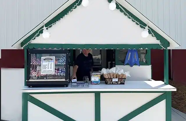 A custom built Christmas food stall with white walls and green accent at a street market with a seller showcasing nuts and other products