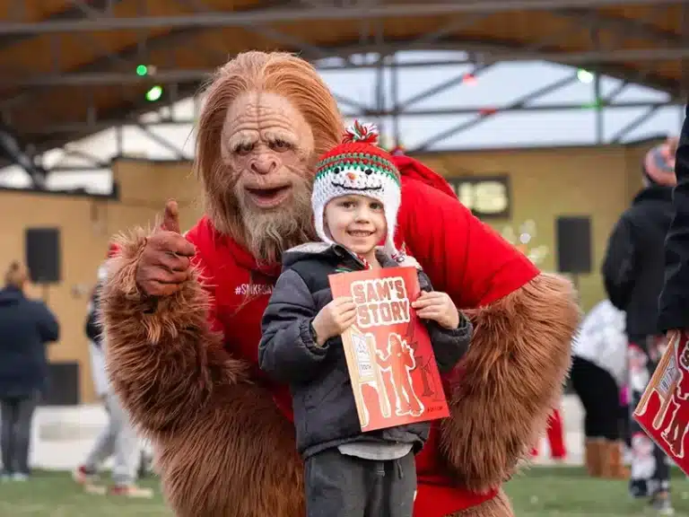 South Milwaukee Sam mascot poses with a young boy with a Sam's Story book at Christmas in the Commons event.