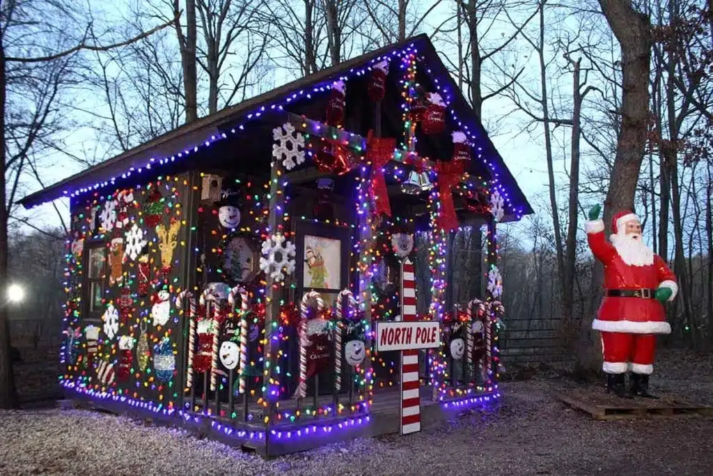 A small building decorated with Christmas decors such as snow flakes, holiday stockings, ribbons and candy canes with a tall Santa Claus sturcture beside it 