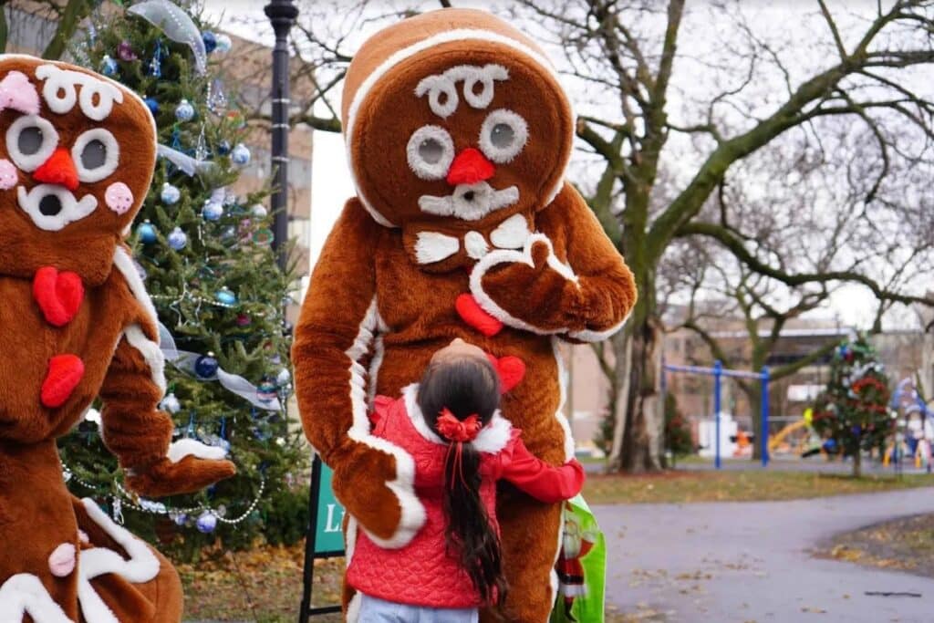 A little girl in red jacket hugging a gian gingerbread mascot during the Cocoa with the Clause at the Cathedral Square Park in Milwaukee.