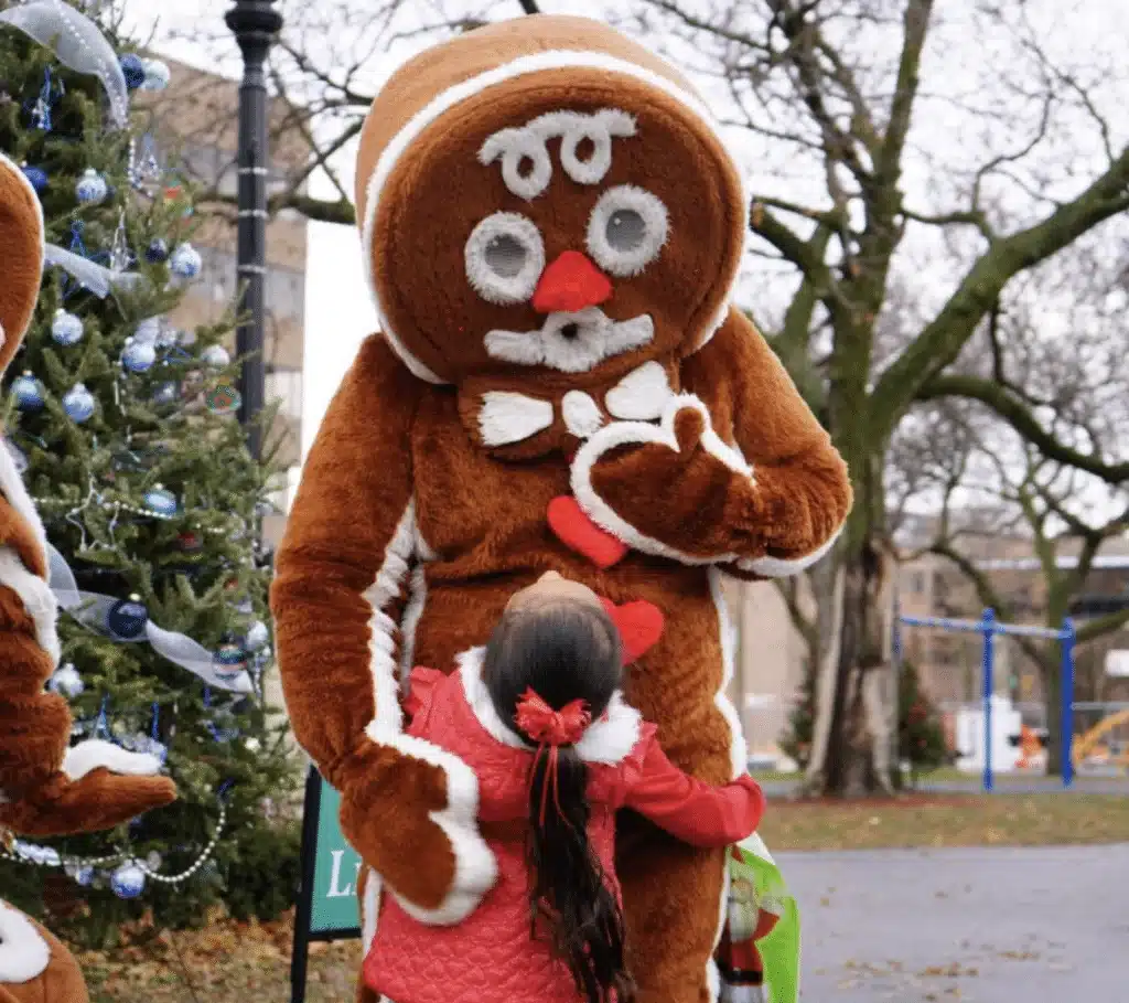 A girl wearing red jacket hugging a gingrebread mascot at the Cathedral Square Park during the Cocoa with the Clauses event
