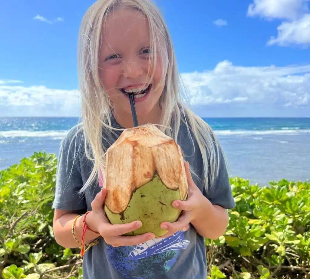 A child drinking coconut water juice straight from the fruit using a black straw