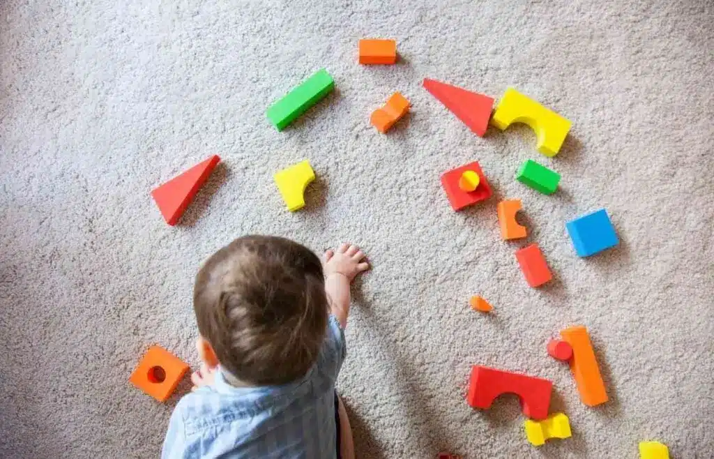 A toddler playing with wooden puzzle pieces in different shapes and colors