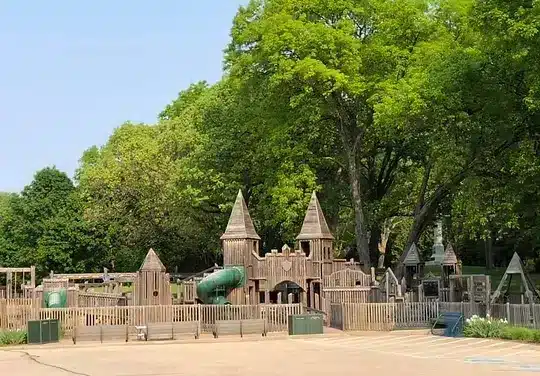 Wooden castle-style playground at Fort Cushing surrounded by tall trees and natural greenery.