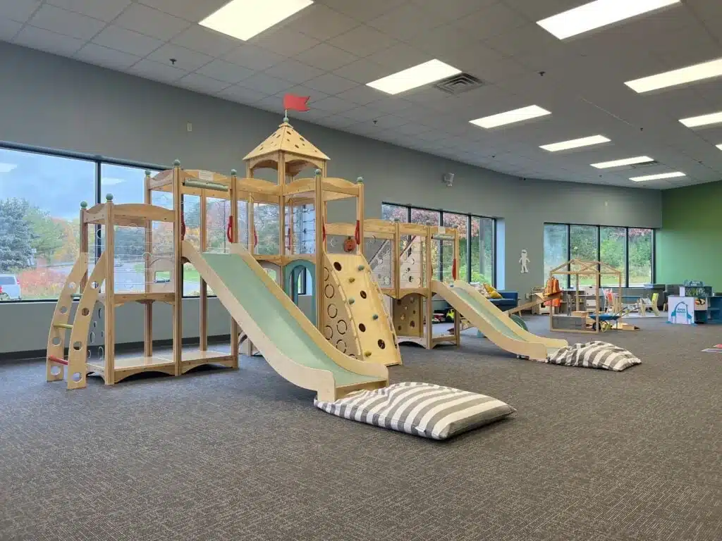 Large wooden climbing structure with slides and padded mats at Bug & Goose Delafield.