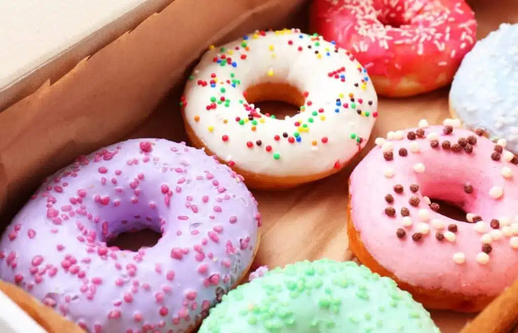 Assorted frosted donuts with colorful sprinkles arranged neatly in a bakery box.