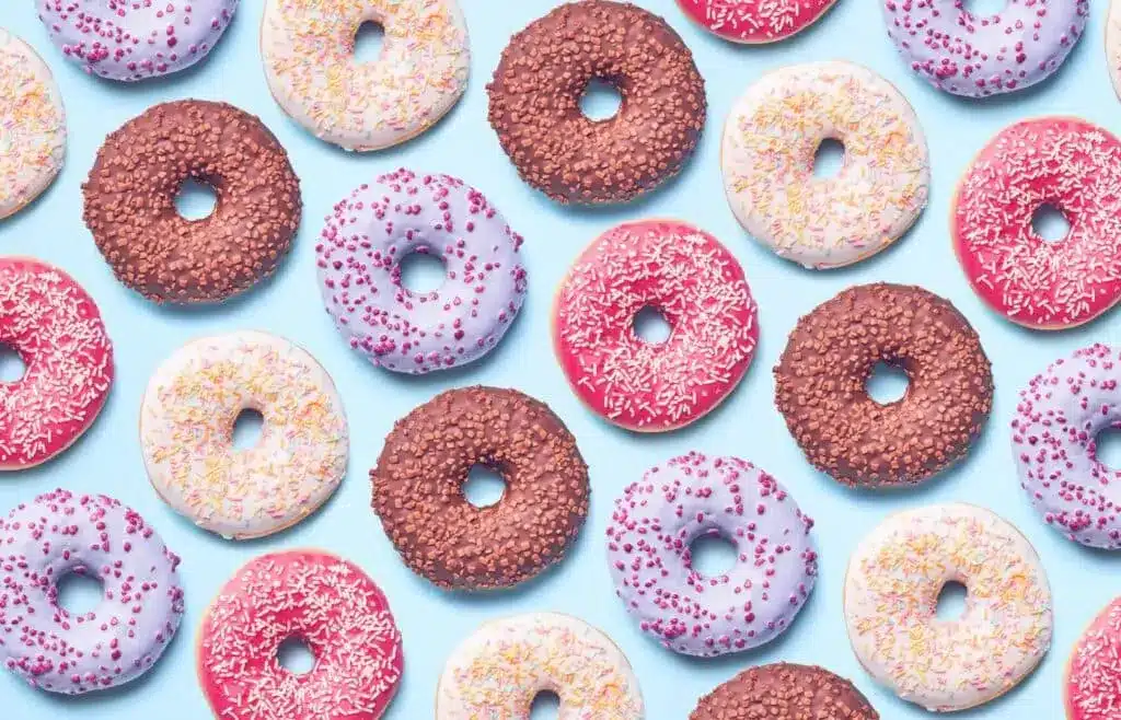 Pattern of colorful frosted donuts with sprinkles arranged on a light blue background.