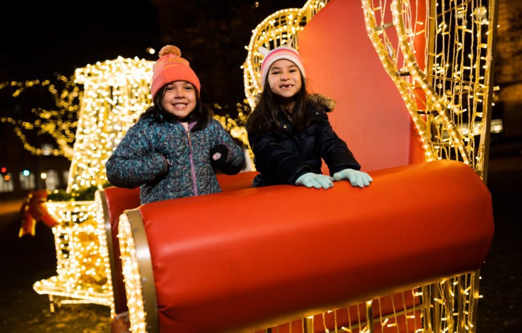 Two girls stting on one of the giant chair display at the Holiday Lights Festival in Downtown Milwaukee.