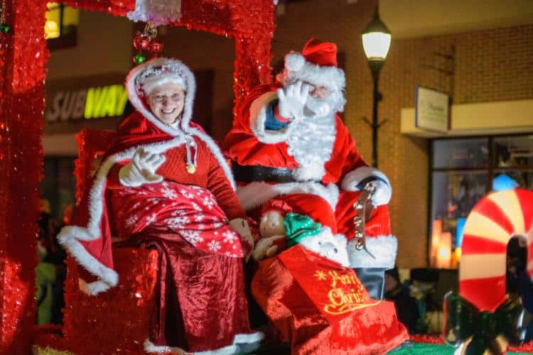 Mrs Clause is smiling at people and Santa is waving while sitting on a red float at the Waukesha Christmas Parade.