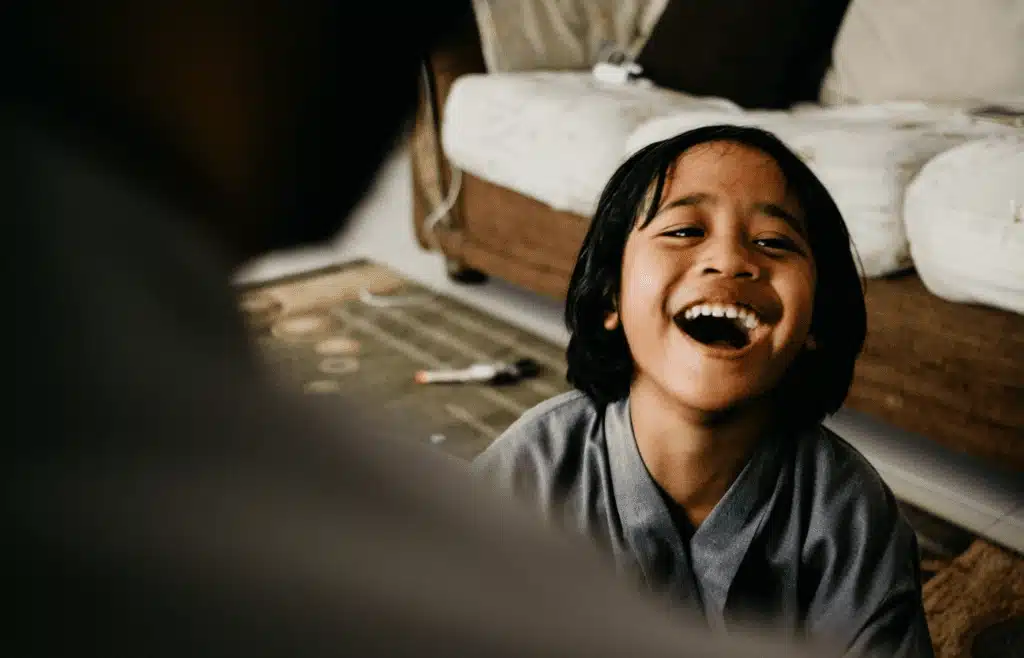 A child sitting indoors, laughing heartily while engaging in a fun conversation with someone