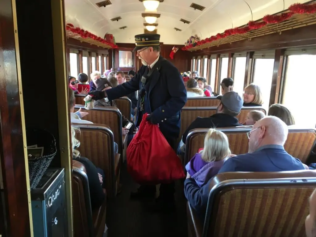 A conductor on the train hands out gifts inside a decorated vintage rail car 