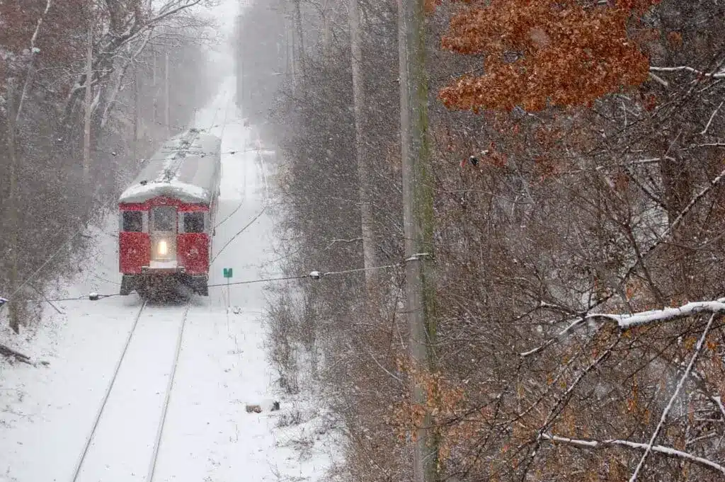 A vintage red East Troy Christmas Train travels through a snowy forest landscape
