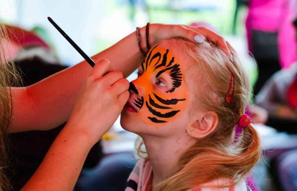 A girl in ponytails having her face painted in orange and black paint