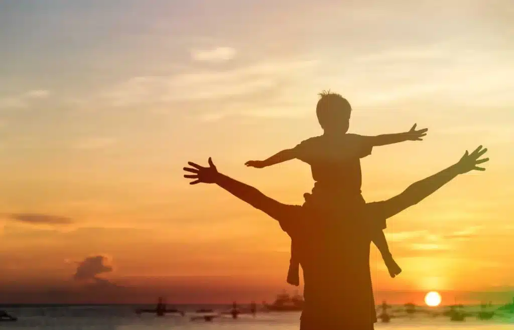 Silhouette of a father carrying his young son on his shoulders with both arms outstretched