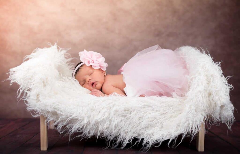 A sleeping baby girl with pink tutu skirt and flower head band and lying on soft white fabric