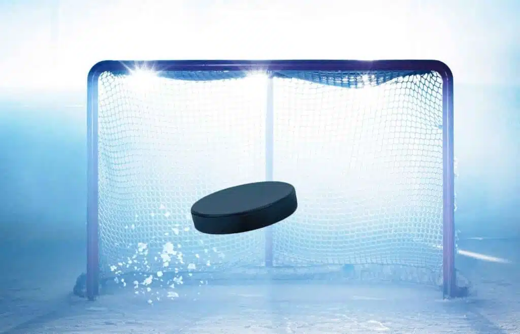 A closeup of black puck as it flies towards the net with stadium lights highlighting the movement.