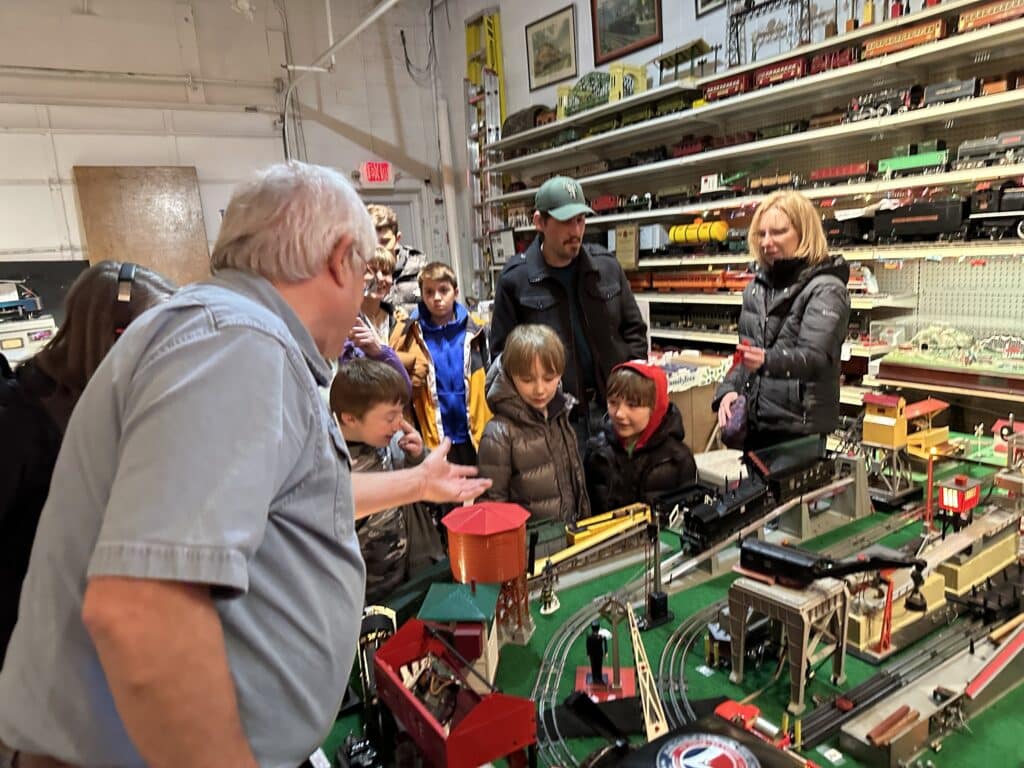 Kids and adults gather around a model train and railroad.