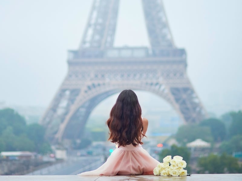 Girl in pink dress and white bouquet and looking at the Eiffel Tower symbolizing classic French girl names
