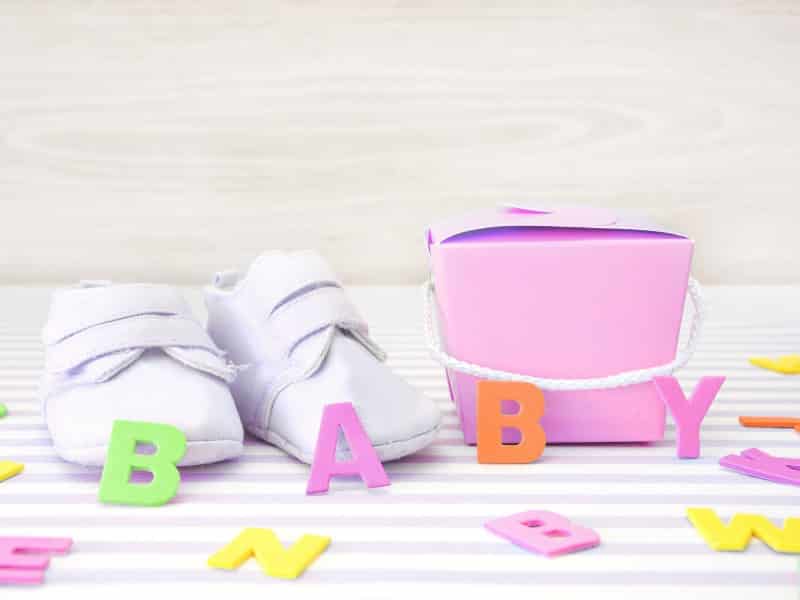 White baby shoes, pink box with wooden letters that say Baby, representing FAQ questions about French girl names