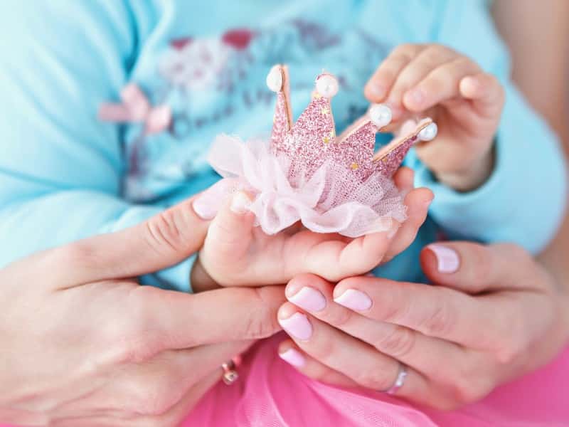 A small girl holding a tiny pink crown and being held by her mother to represent French girl names with strong meanings