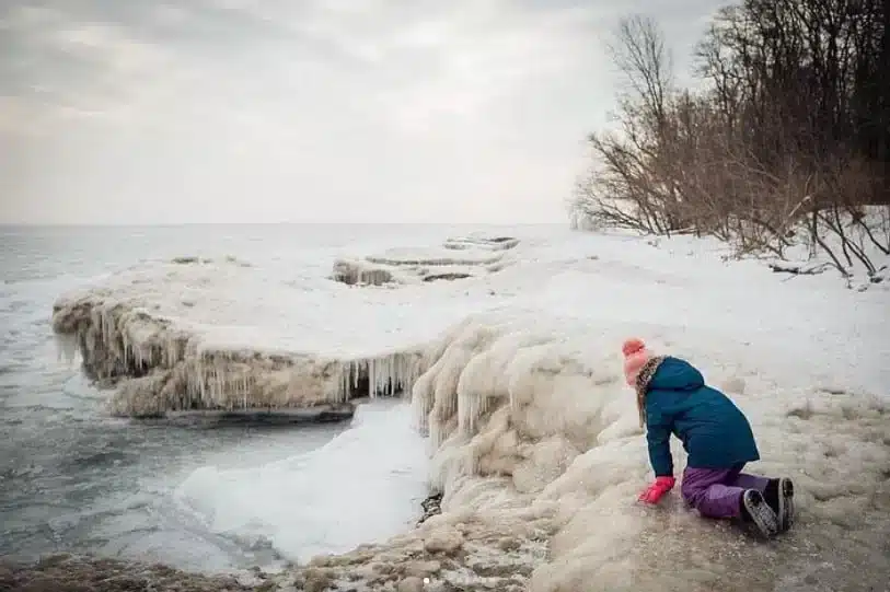 Girl in blue jacket and pink gloves checking the ice formations at Schlitz Audubon Nature Center during winter
