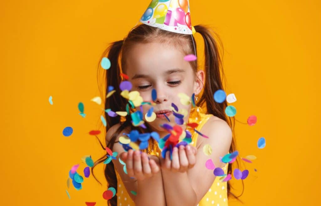 A girl with party hat blowing confetti during a birthday party
