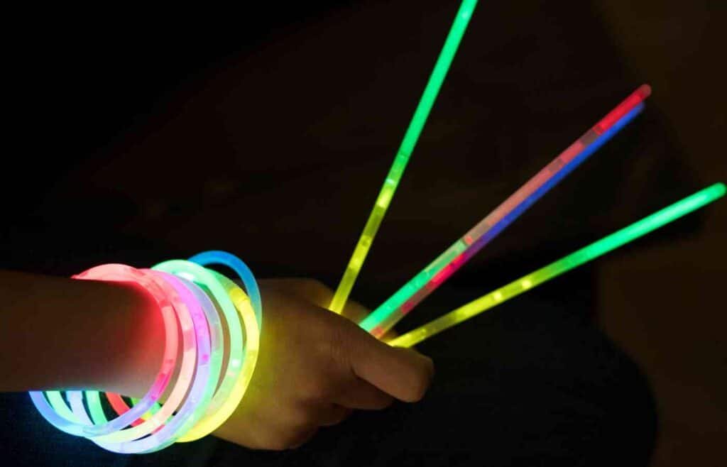 A hand with a glowstick bracelet and also holdiong three glow sticks