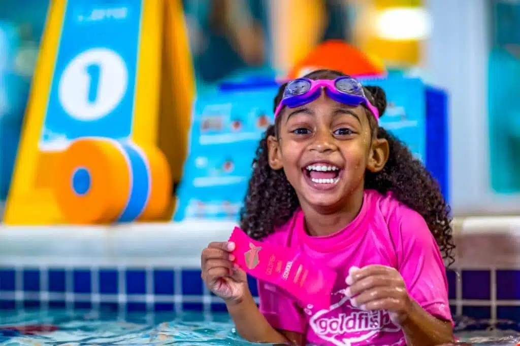 A girl with curly hair and fuschia rash guard is smiling to the camera