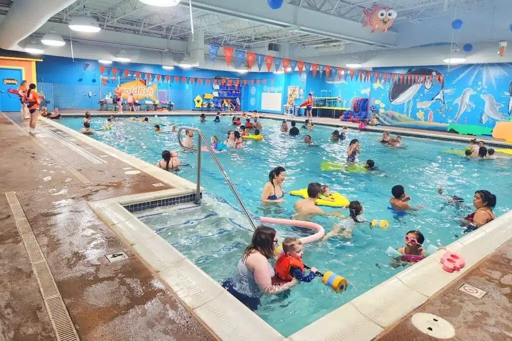 Several children with their adult companions swimming in a large pool