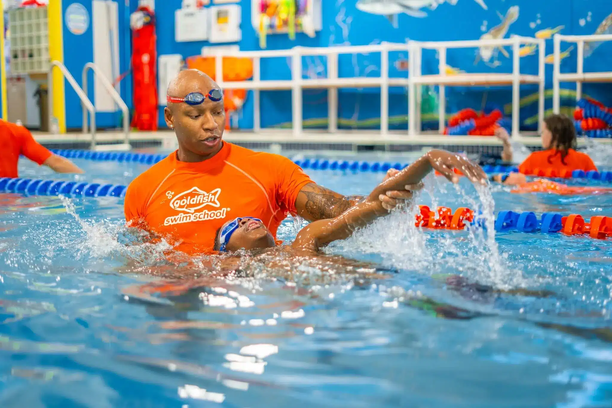A Goldfish Swim School coach is guiding a swimmer on proper backstroke techniques