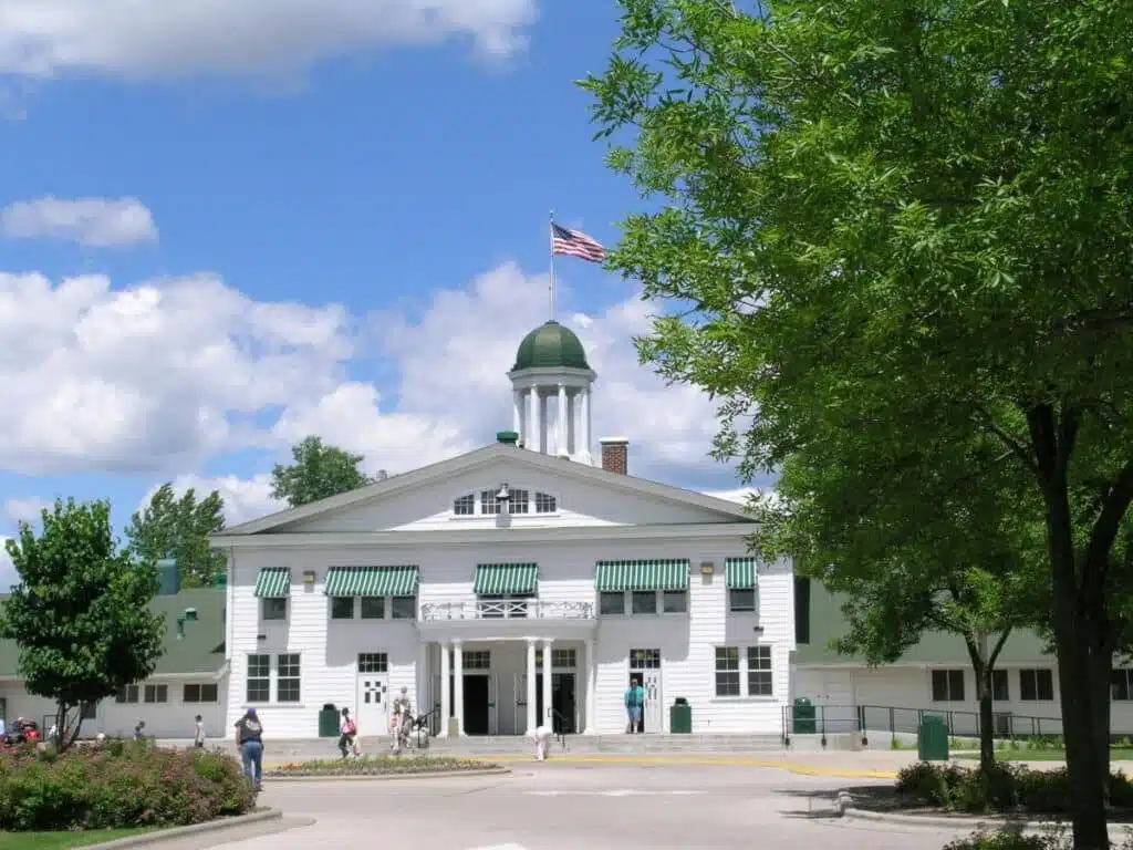 White building with green awnings and an American flag flying above the dome on a bright summer day.