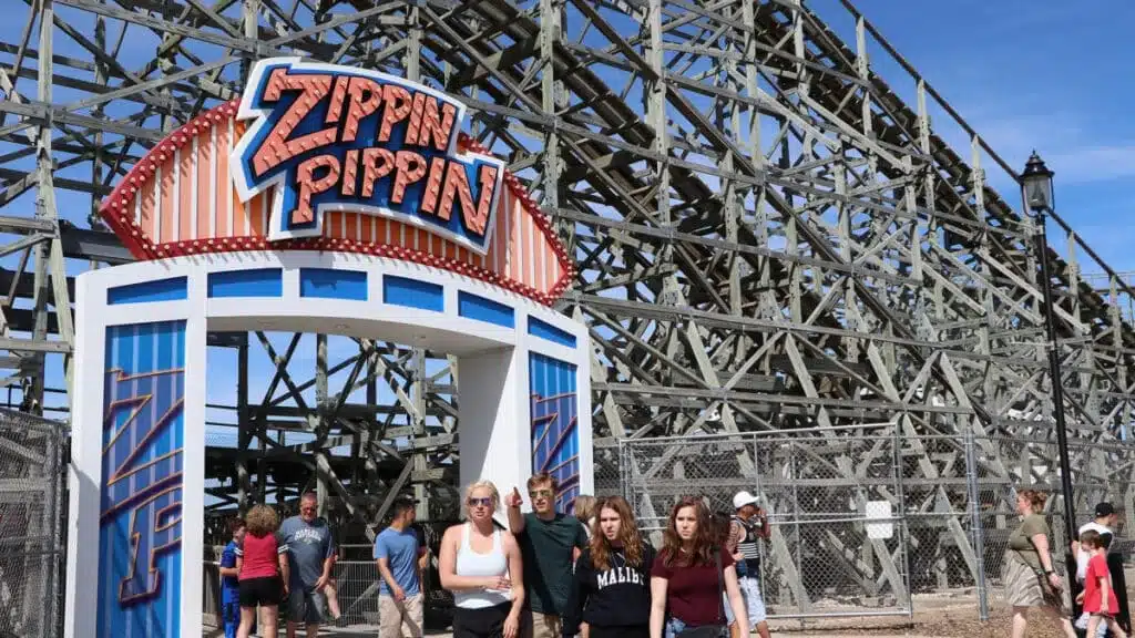 Families at the entrance sign of the Zippin Pippin wooden roller coaster  with the towering wooden track 