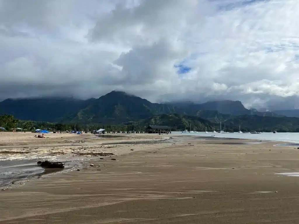 Beach front with a pier and mountains partially covered by clouds in the background
