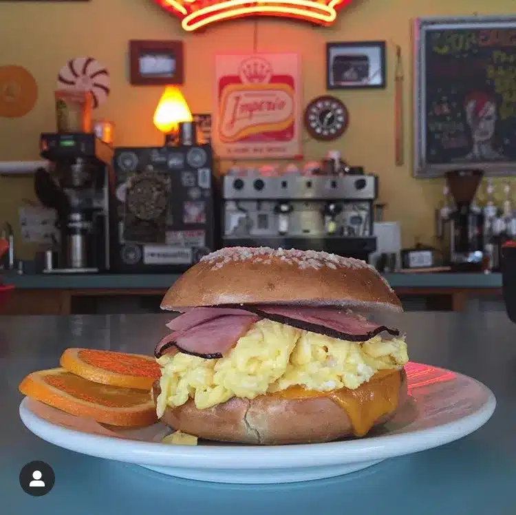 A closeup of a breakfast burger with ham. egg and melted cheese with two slices of oranges on the side