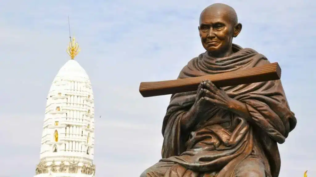 Statue of Mahatma Gandhi with a white temple structure in the background.
