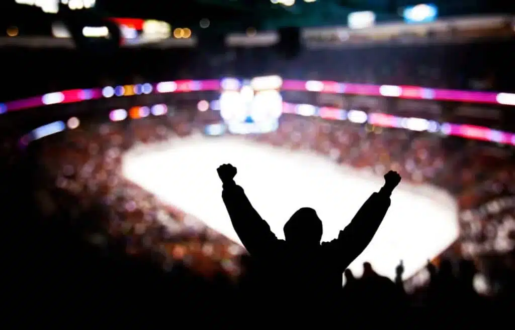 Silhouette of a hockey fan raising his arms as sign of celebrating a goal