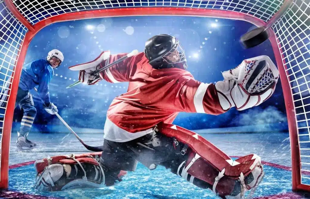 Goalie in red gear diving to stop the puck from getting inside the net.