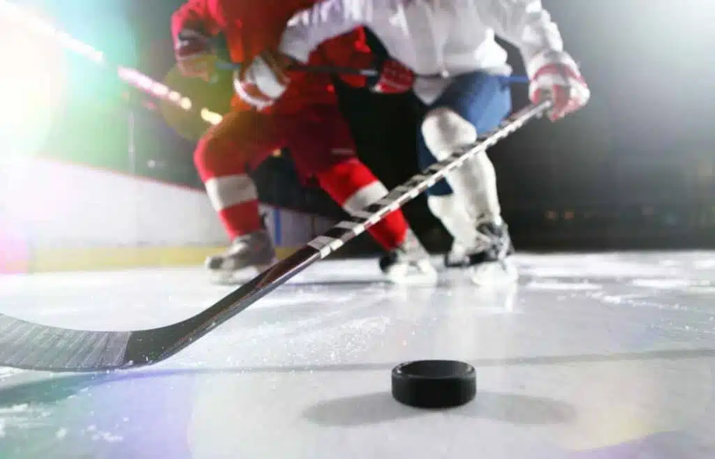 Two opposing hockey players trying to control the movement of the puck on ice.